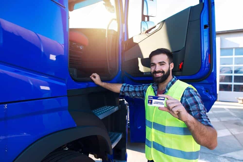 A truck driver holding his Class B CDL in his left hand while boarding the truck looking at the camera
